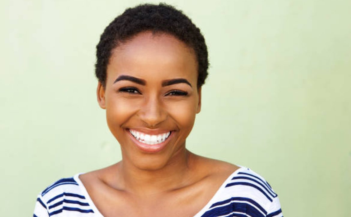 Close up portrait of young black woman smiling against green wall